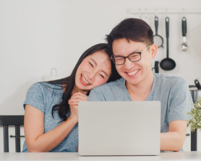 Young Asian couple enjoy shopping online on laptop at home. Lifestyle young husband and wife happy buy ecommerce after have breakfast in modern kitchen at house in the morning concept.